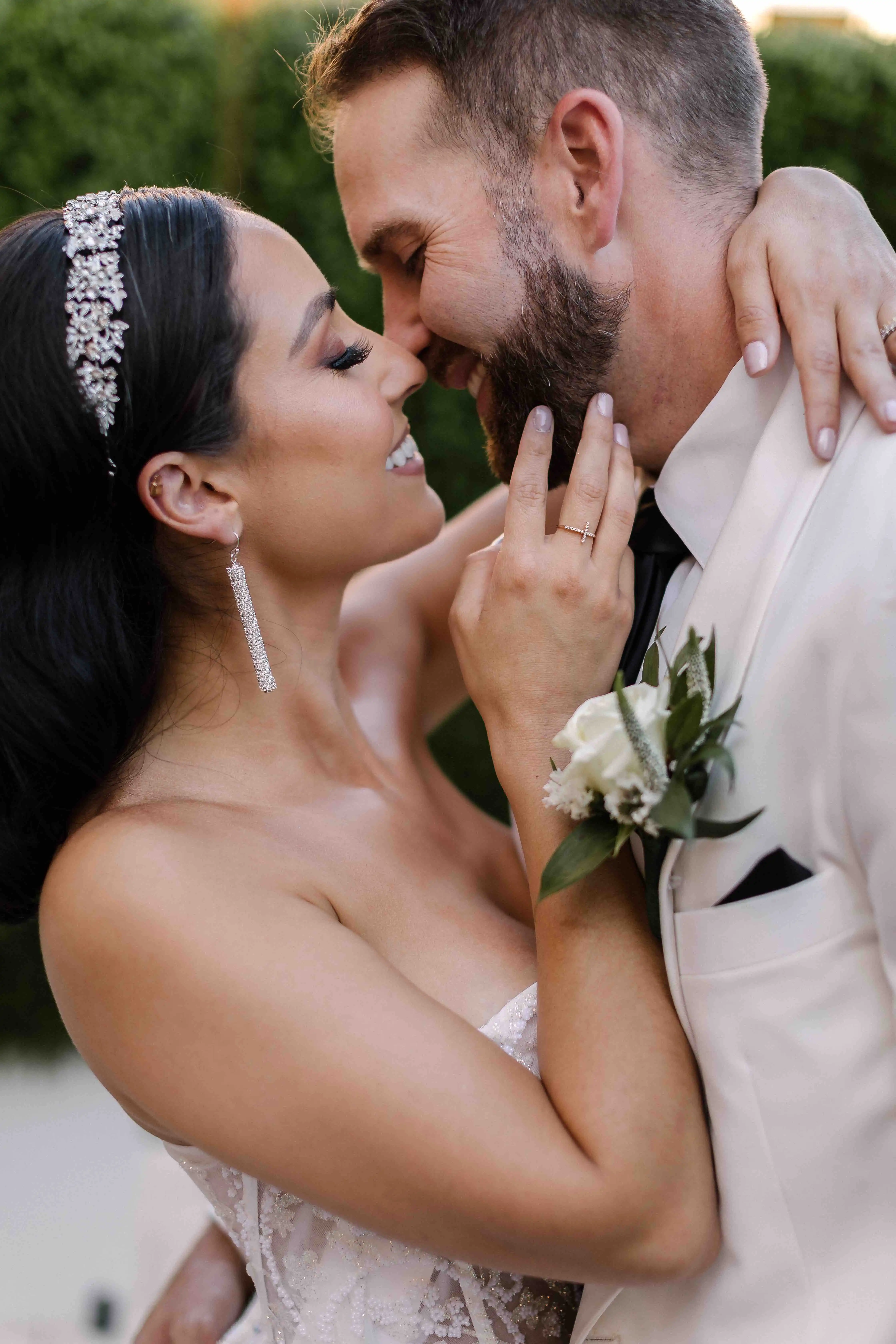 Bride and groom in an embrace with eyes closed, smiling, and touching noses intimately.