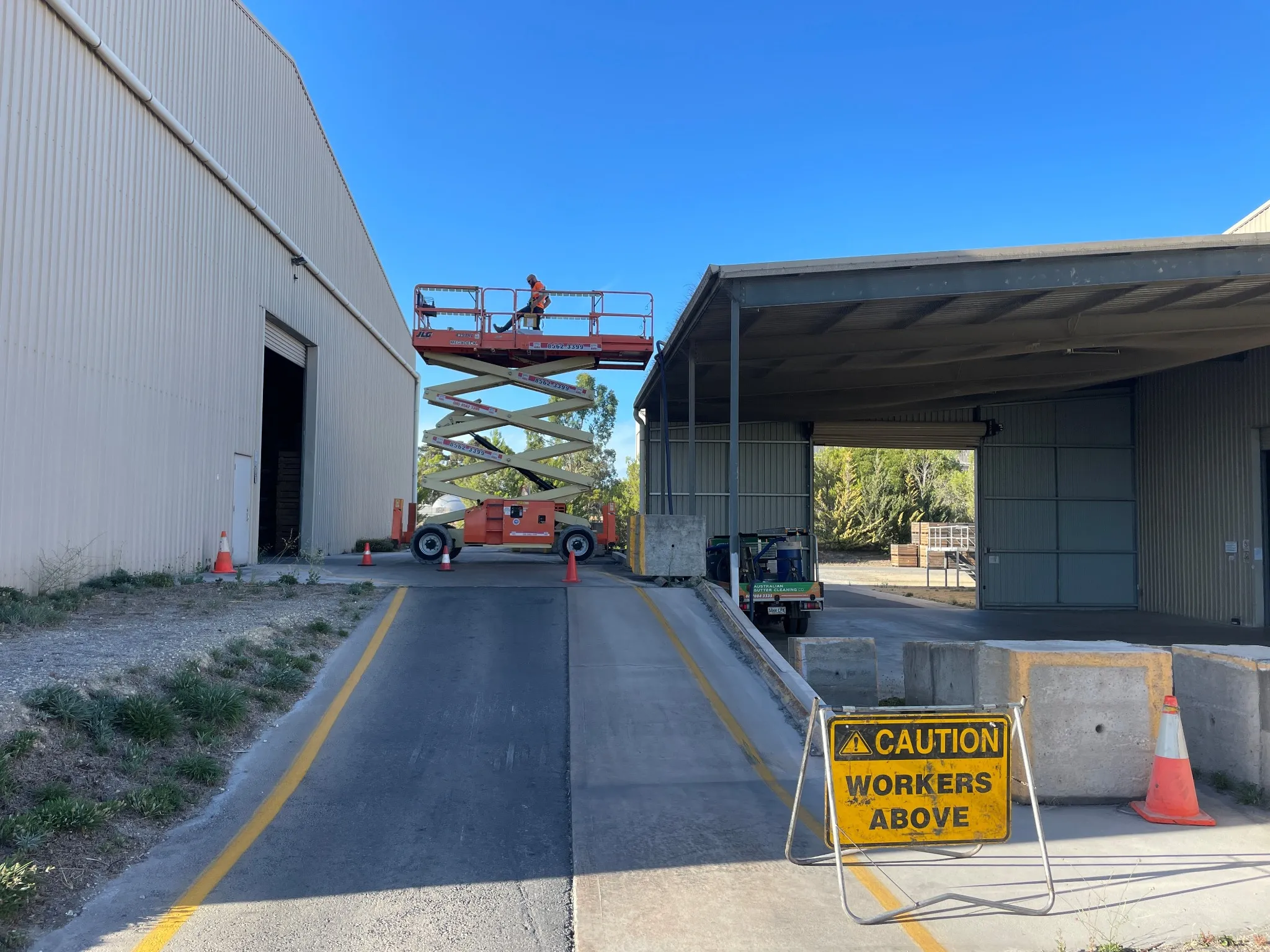 An AGCCO crew using a scissor lift beside a commercial building, with cones and warning signage.