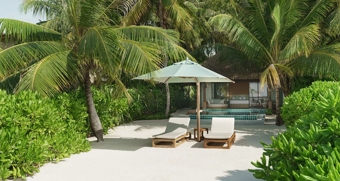 Pool der Huvafen Fushi Beach Villa mit Sonnenschirmen und Blick auf das Meer.