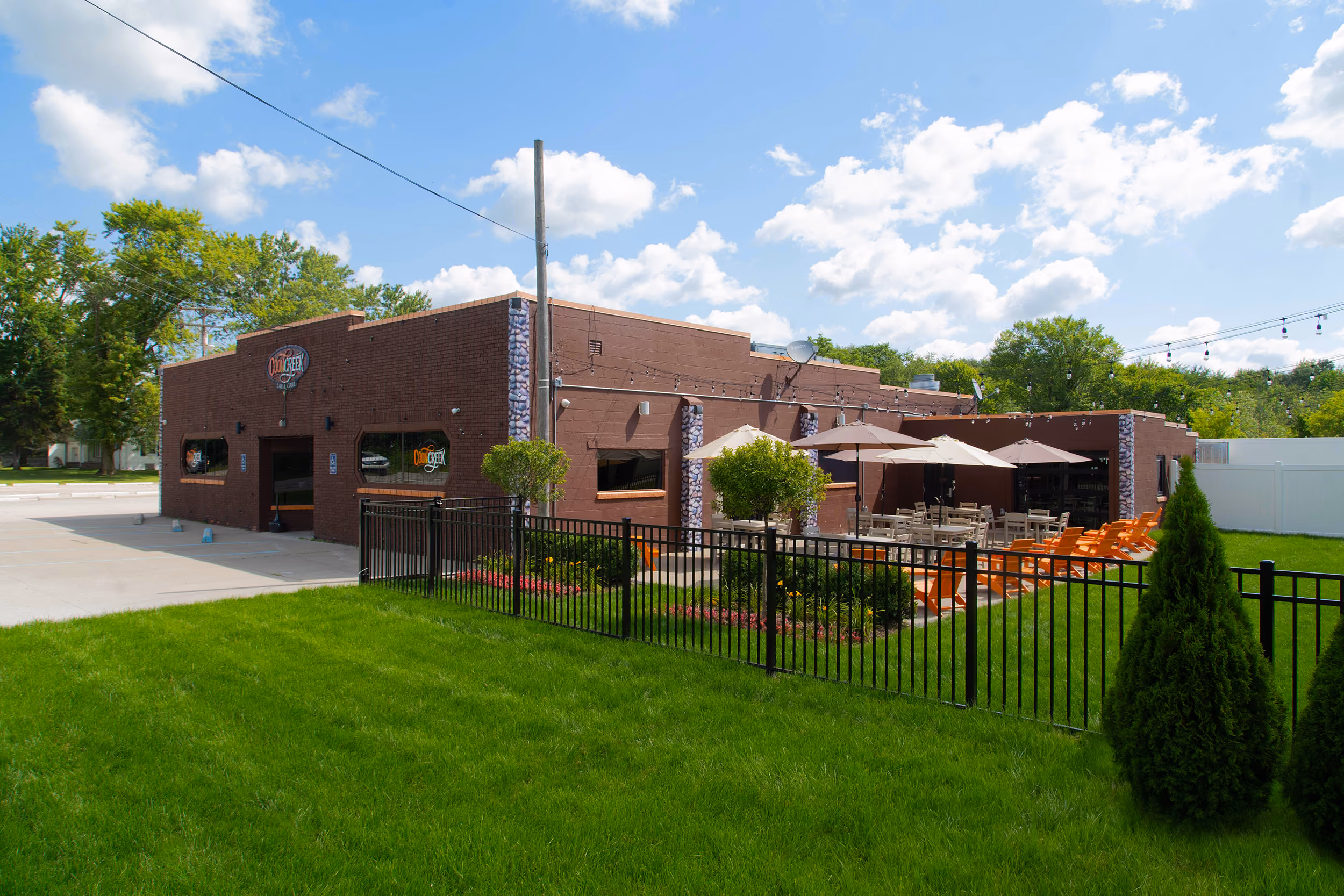 Coon Creek Steakhouse with outdoor patio seating under umbrellas and orange chairs, fenced grassy area.