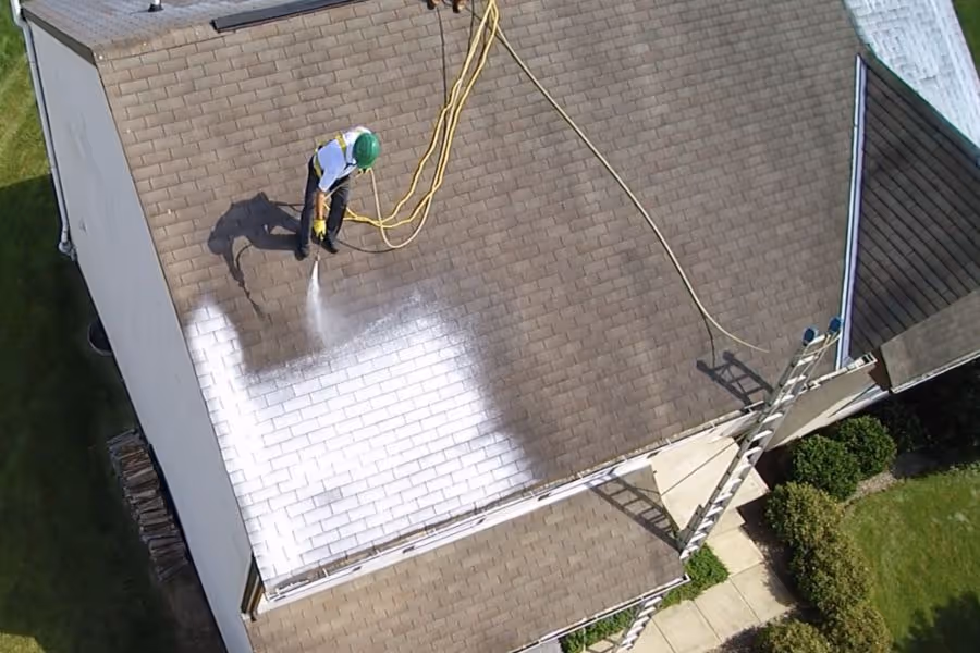 The great restoration continues in this scenic image, showcasing a man diligently spraying a roof restoration solution onto asphalt shingles. This cost-effective approach to roof replacement offers homeowners a chance to rejuvenate their roofs and prevent water damage. 