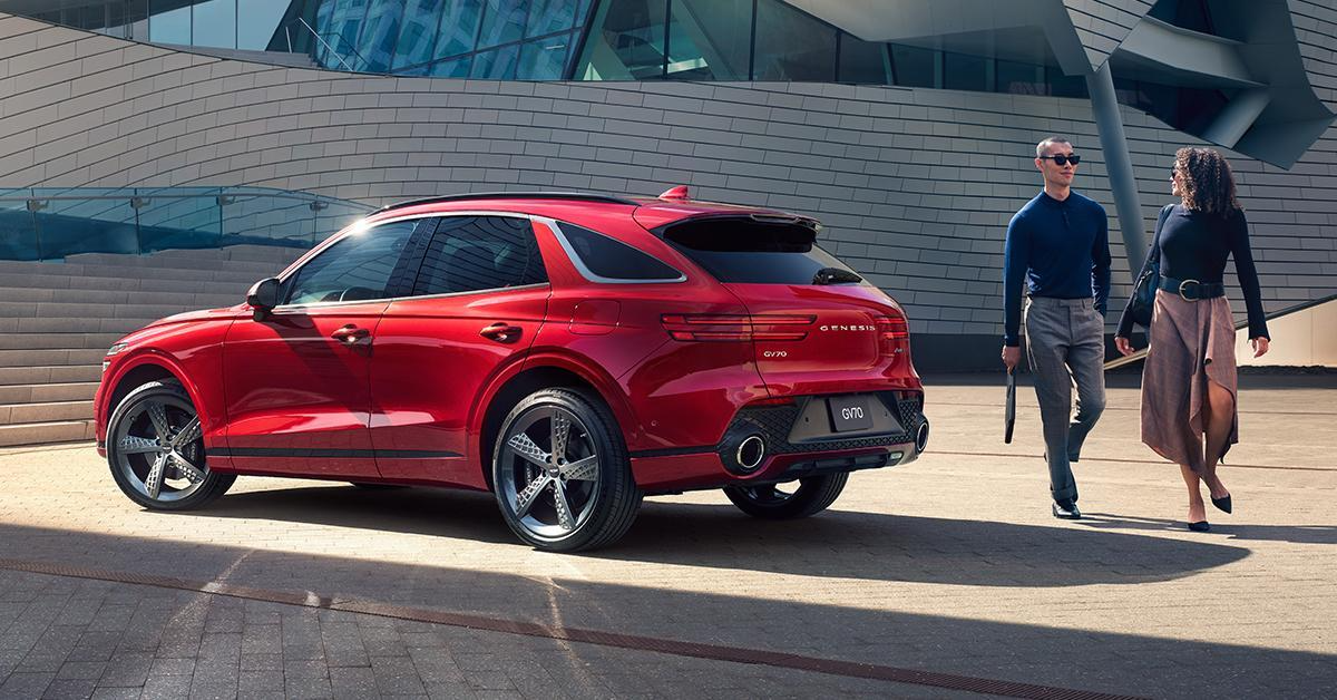 A man and a woman walk next to a Genesis GV70