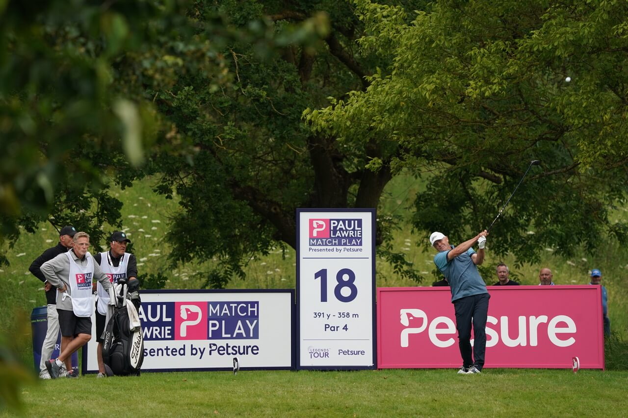 Golfer teeing off at the 18th hole with Petsure branding and caddies watching at the Paul Lawrie Match Play.