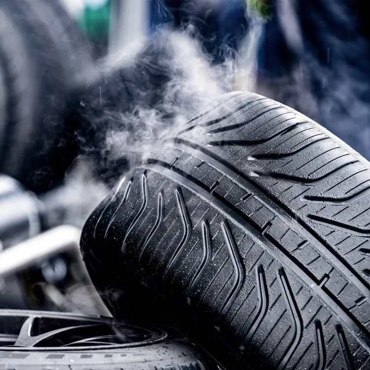 Close-up of a steaming race car tire with visible tread patterns in a workshop setting.