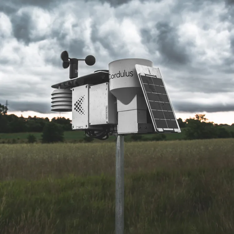 Cordulus weather station mounted on a pole in a grassy field with cloudy sky in the background.