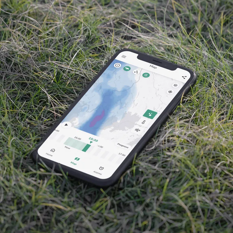 Smartphone on grass showing the cordulus farm weather app with a precipitation map and forecast timeline.