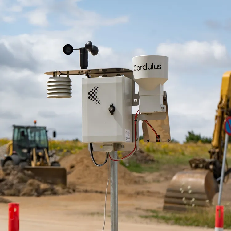 Cordulus weather station with anemometer, solar panel, and rain gauge mounted on a metal pole in a rural field.