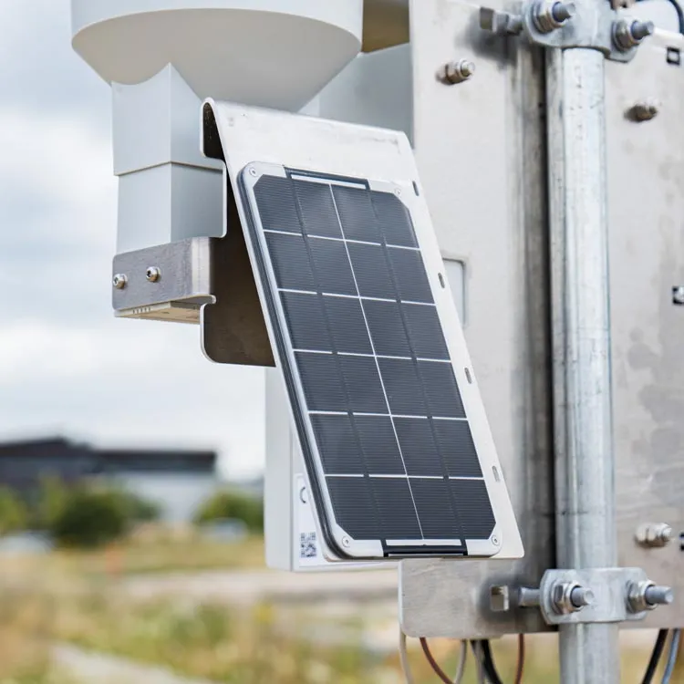 Small solar panel mounted on metal bracket attached toa cordulus site weather station with a blurred background of greenery and sky.