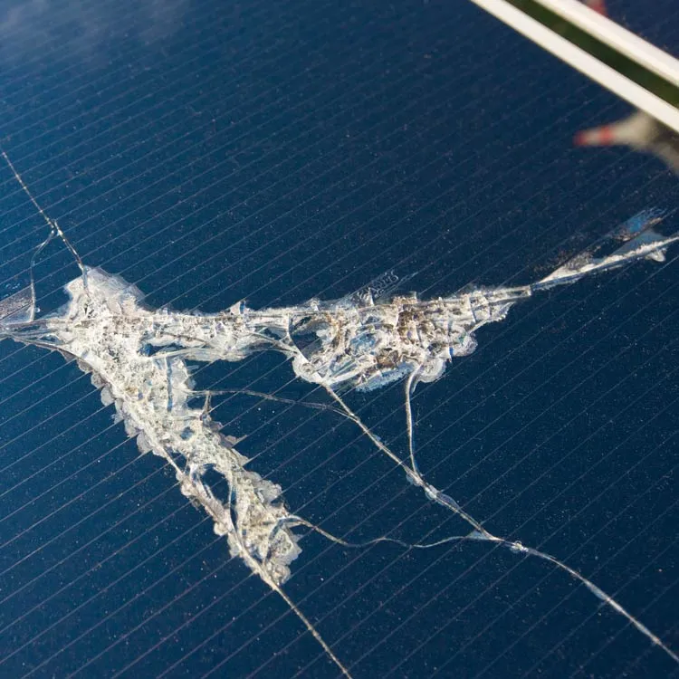 Close-up of a car windshield with a large cracked and shattered area, with impact damage from hail or a storm.