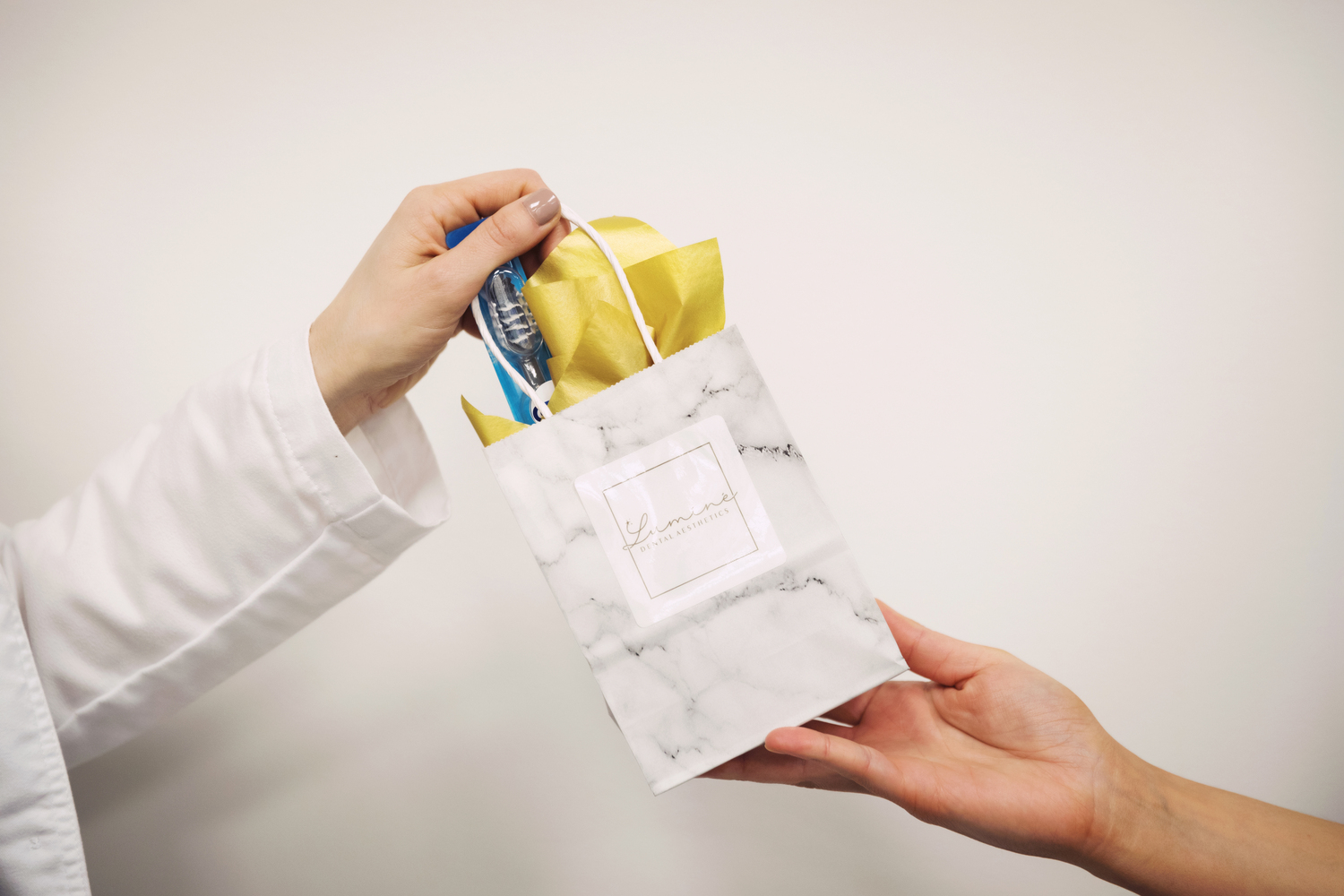 Dentist handing a patient a gift bag with a toothbrush and dental care products at Luminé Dental Aesthetics office