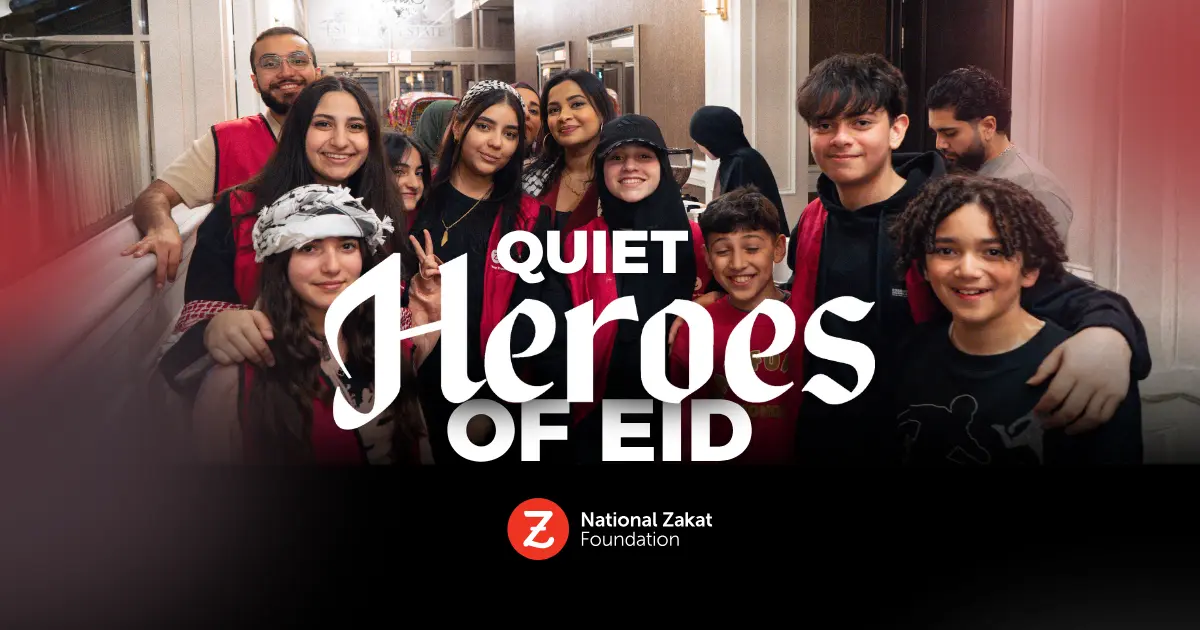 Group of smiling people, including children and adults, gather wearing red vests. Text reads "Quiet Heroes of Eid" with National Zakat Foundation logo.