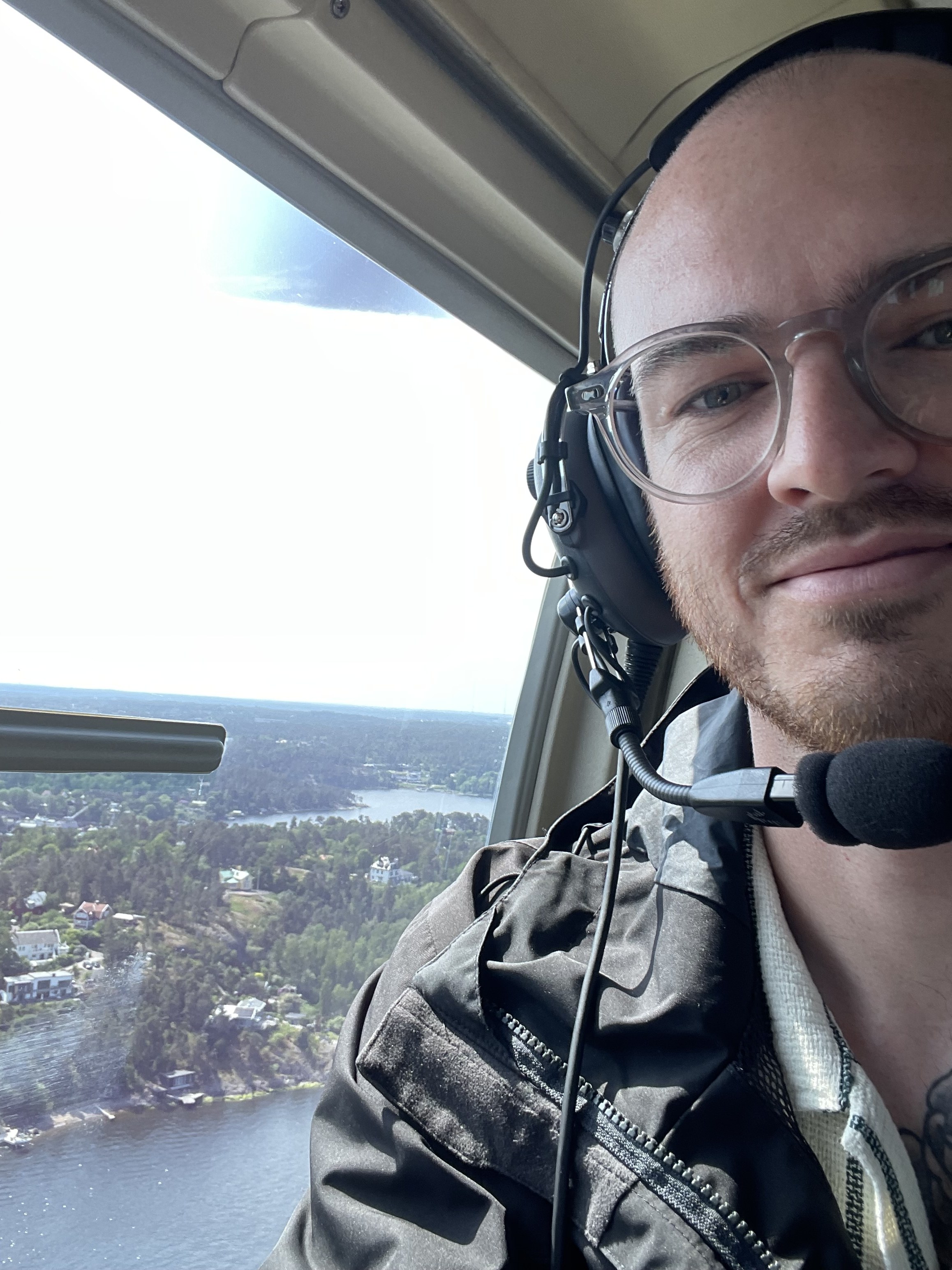 Mikael Beventorp in an aviation headset and glasses, smiling by an aircraft window above islands and water