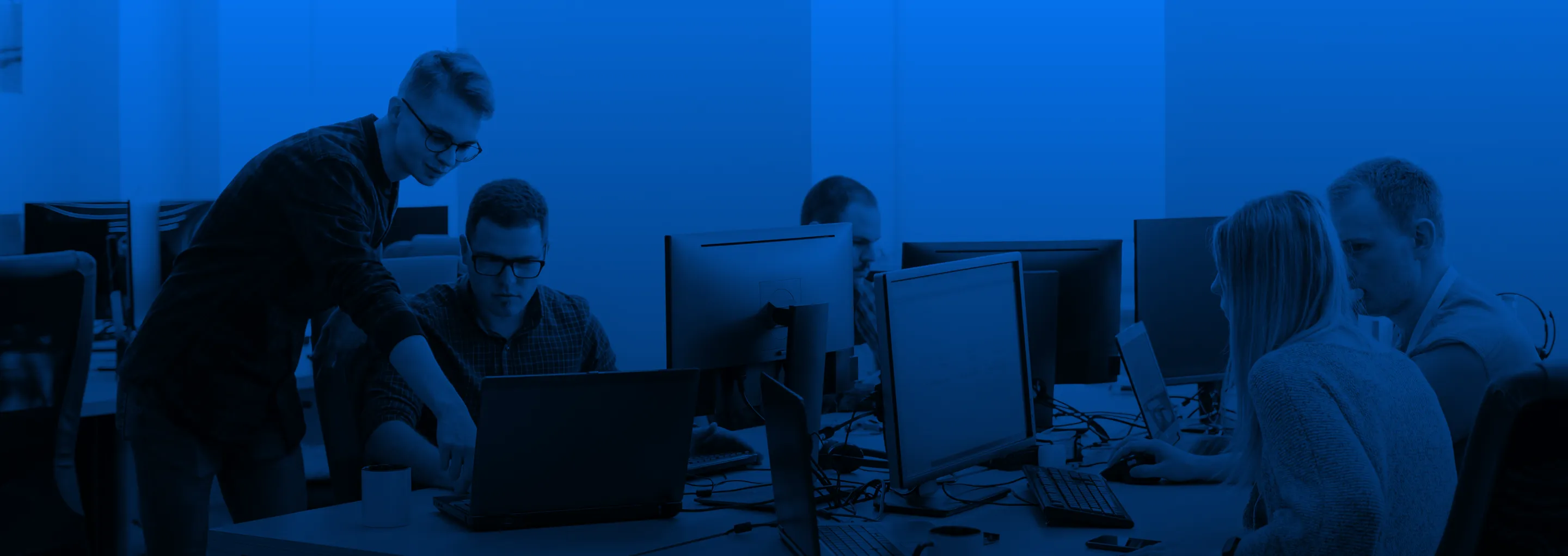 Team of software developers working together at computers in an office setting.