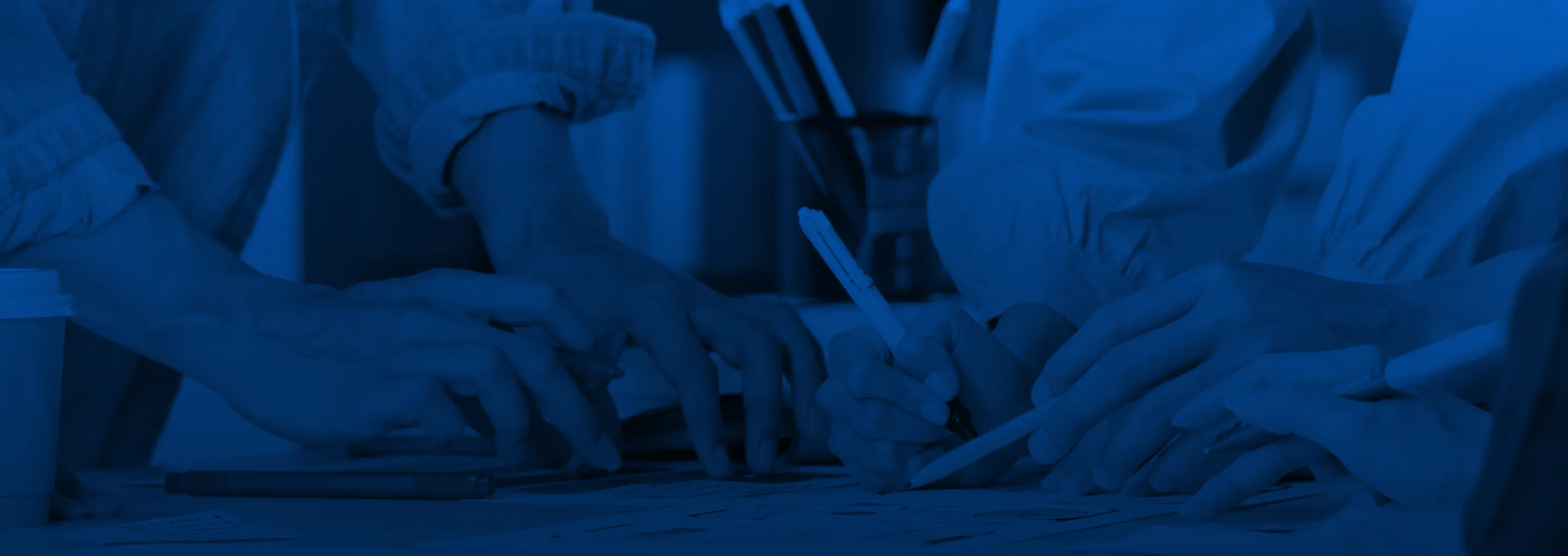 Close-up of a team collaborating over documents on a table with a dark blue color overlay.