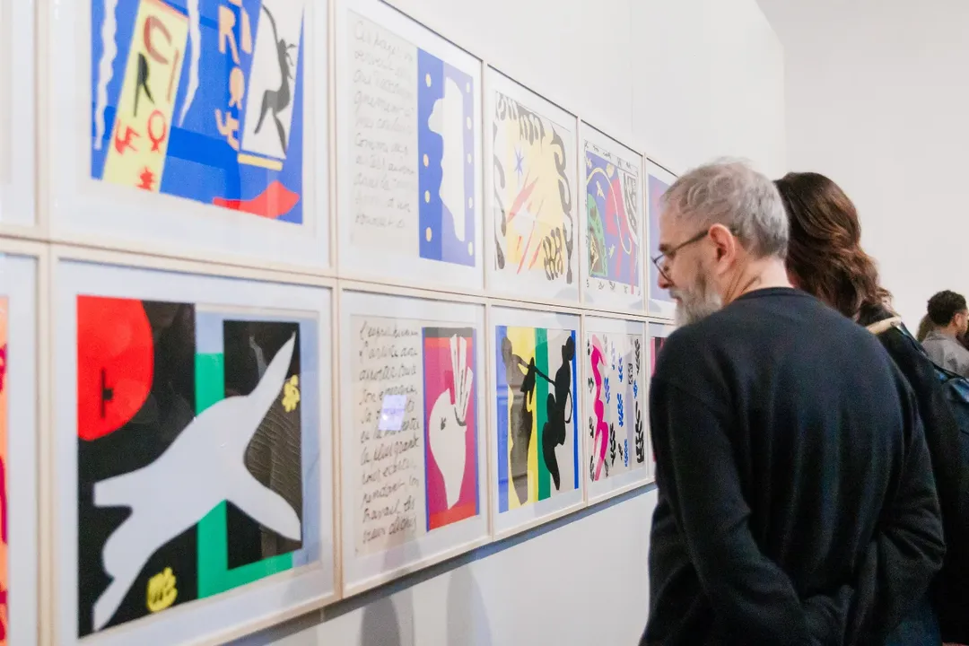 A imagem é uma foto de um homem de perfil observando um quadro que está à sua esquerda. 