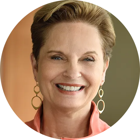 Smiling middle-aged woman with short light brown hair wearing gold oval earrings and a coral blouse.