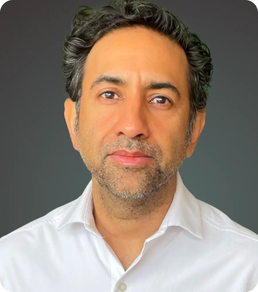 Portrait of a man with dark curly hair, slight beard, wearing a white shirt, against a gray background.