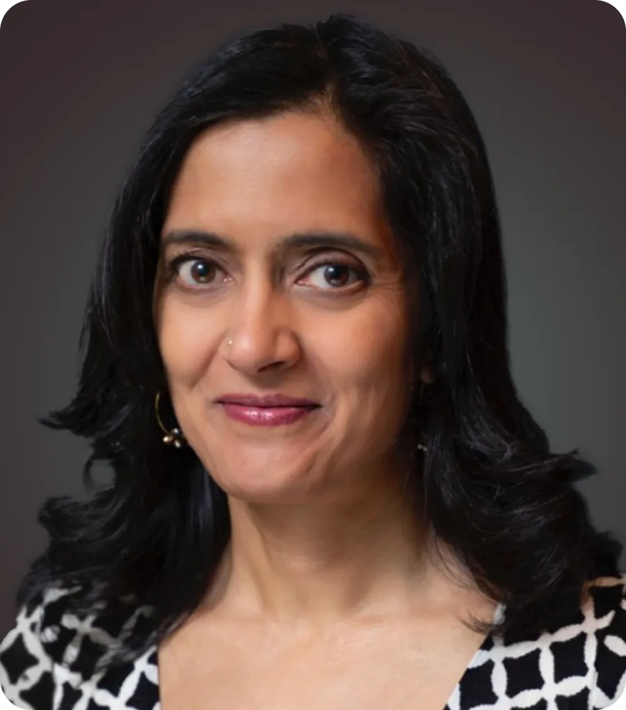 Portrait of a woman with medium-length black hair, wearing a black and white patterned top and gold hoop earrings.