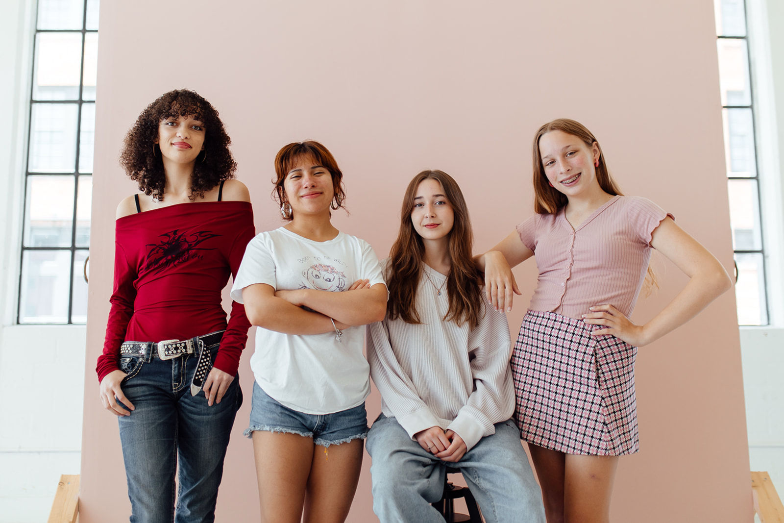 Group of 4 teens standing against the wall in a studio space, smiling and feeling comfortable in therapy.