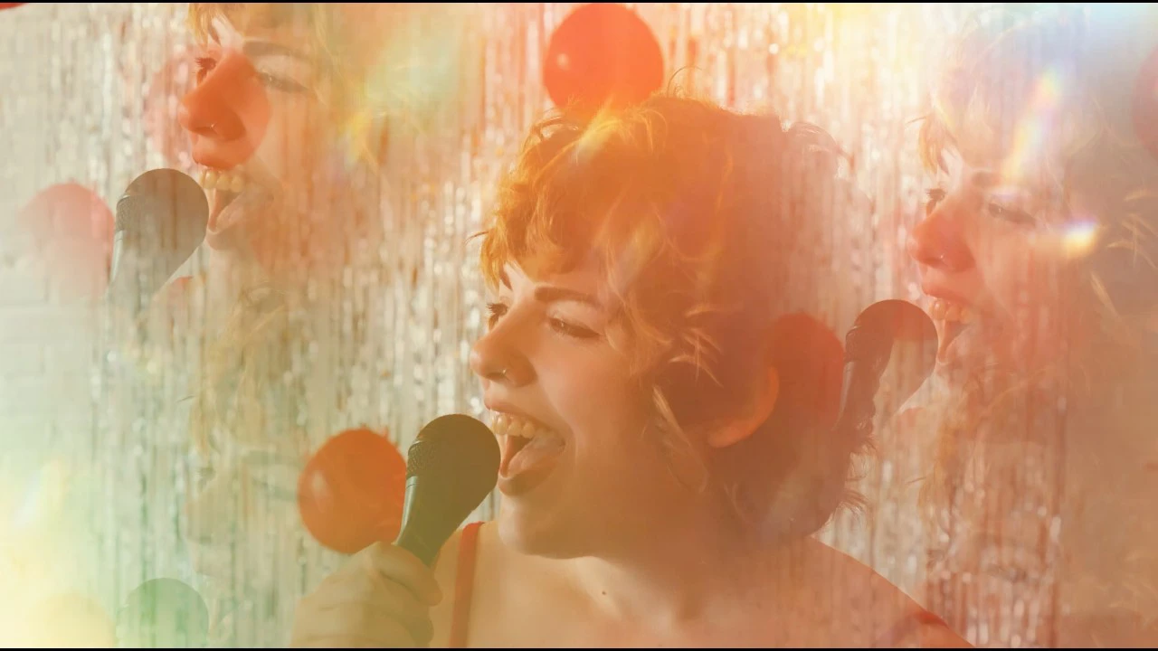 A hazy, kaleidoscoping headshot of Jill singing into a mic while looking off to the left in front of shimmering streamers