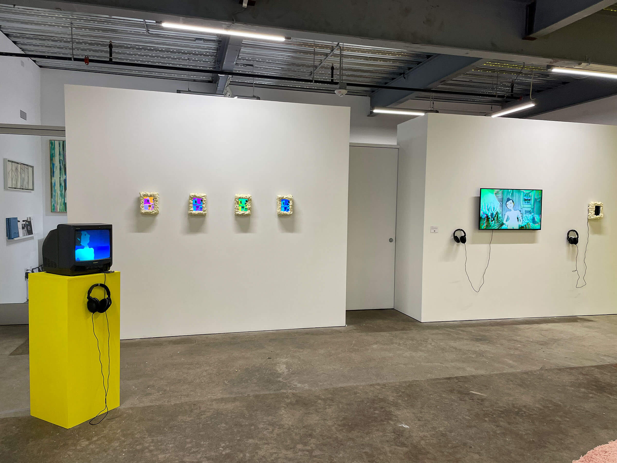 Installation view of 'SUPERPROMPT', showing a white wall with a row of small moulded TV screens playing animations are set up