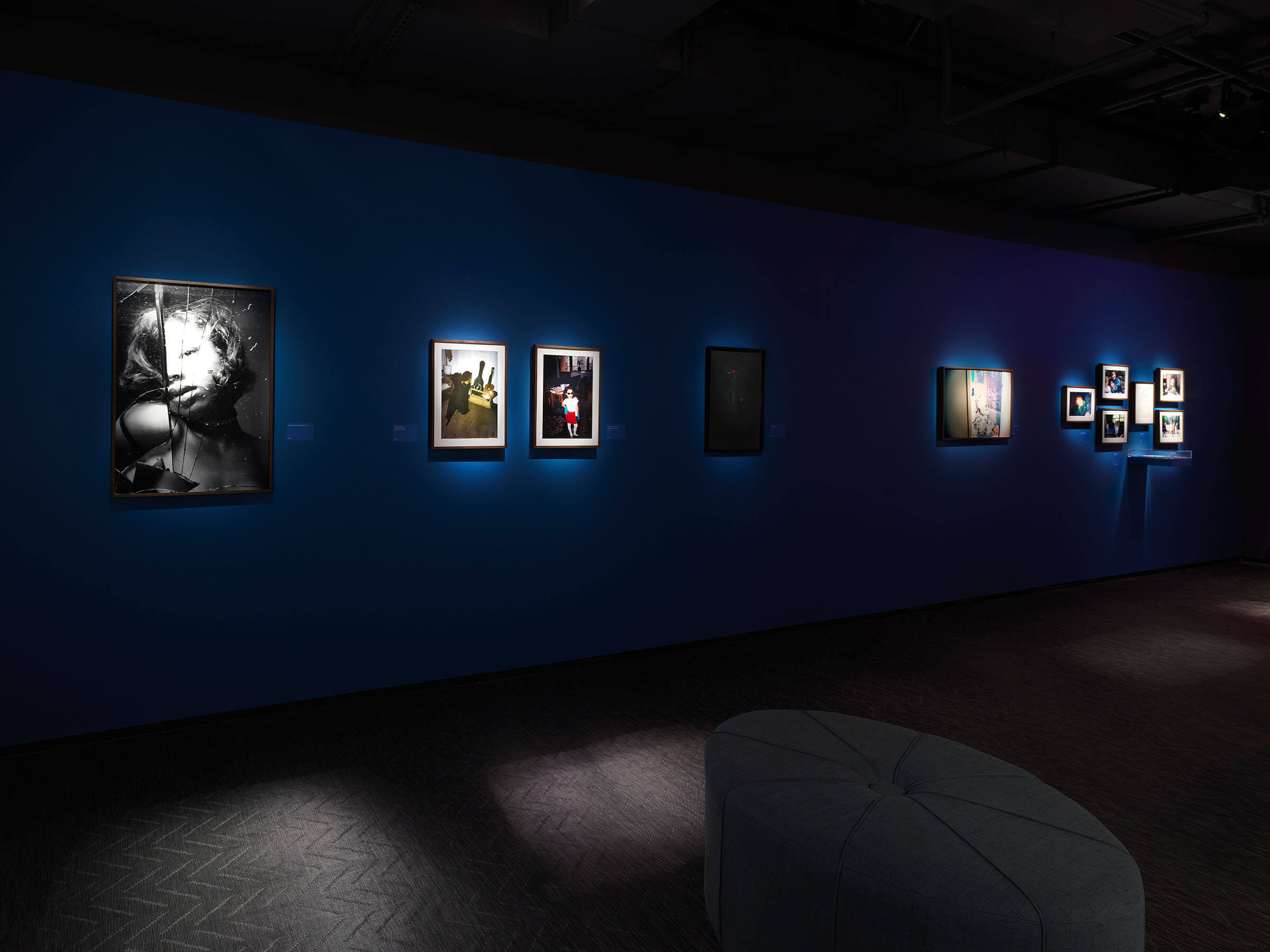 A black and white printed photograph of Kia LaBeija's reflection in a cracked mirror is displayed next to old family photos on a dark blue wall