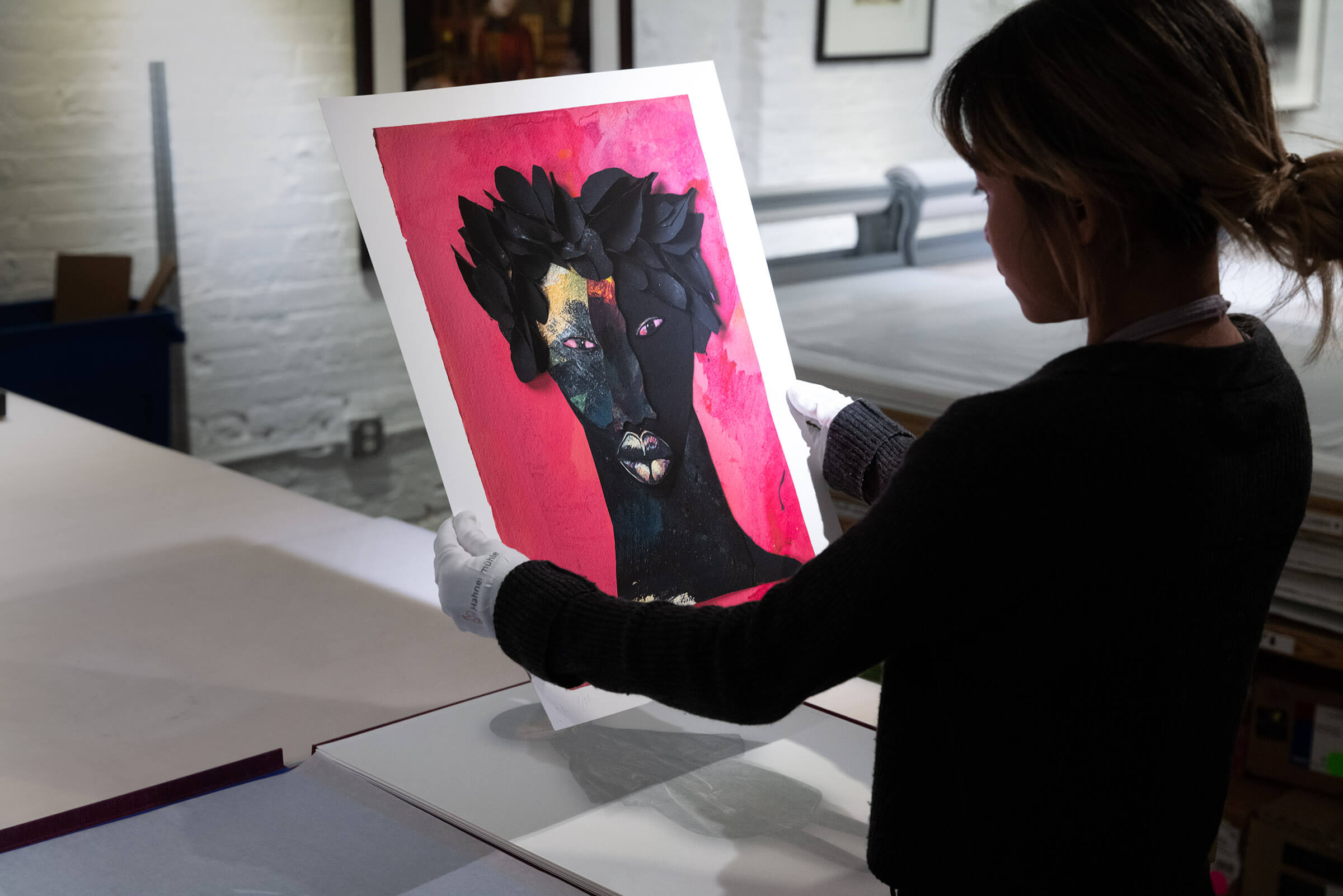 Holding up 'Timbuktu' by Barbara Bullock, a collage of a black figure portrait made out of painted black leaves against a hot pink painted background