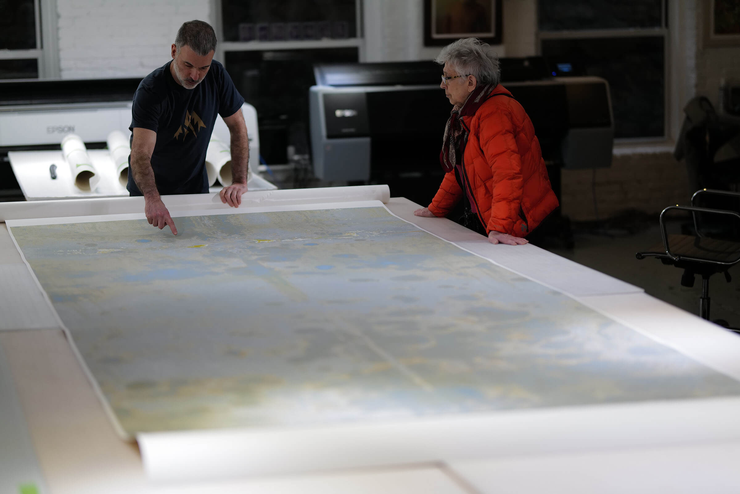 Reeva Potoff in the studio looking at final prints of her '8Veil & B&G mold & GreyStucco' series out on a table