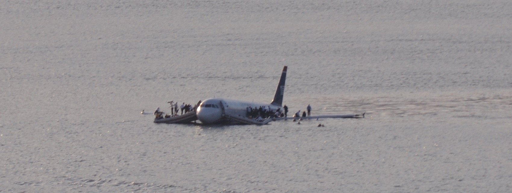 US Airways Flight 1549 floating low in the Hudson River, passengers standing on both wings and in inflatable rafts alongside the fuselage.