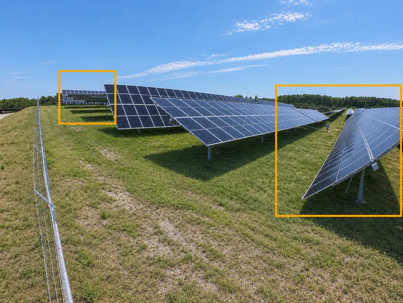 Rows of dark blue solar panels stretch across a grassy, fenced field under a clear sky; orange boxes highlight panels at both ends, creating a calm, orderly scene.