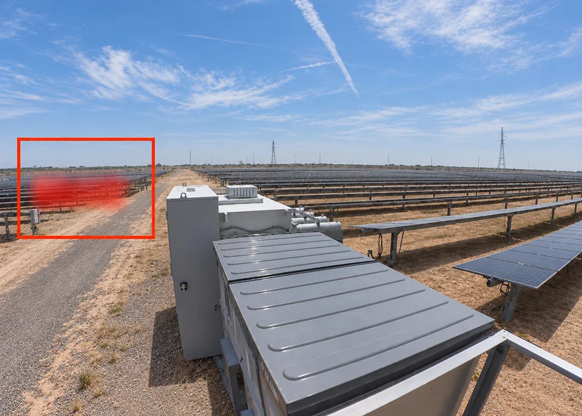A solar farm stretches across a dry landscape beneath a bright blue sky; a red box highlights a blurred red object near the left edge.