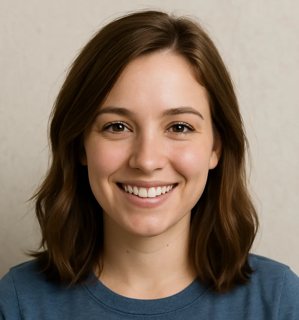 A young woman with shoulder-length brown hair smiles warmly at the camera, wearing a blue shirt. The background is a neutral, light color.