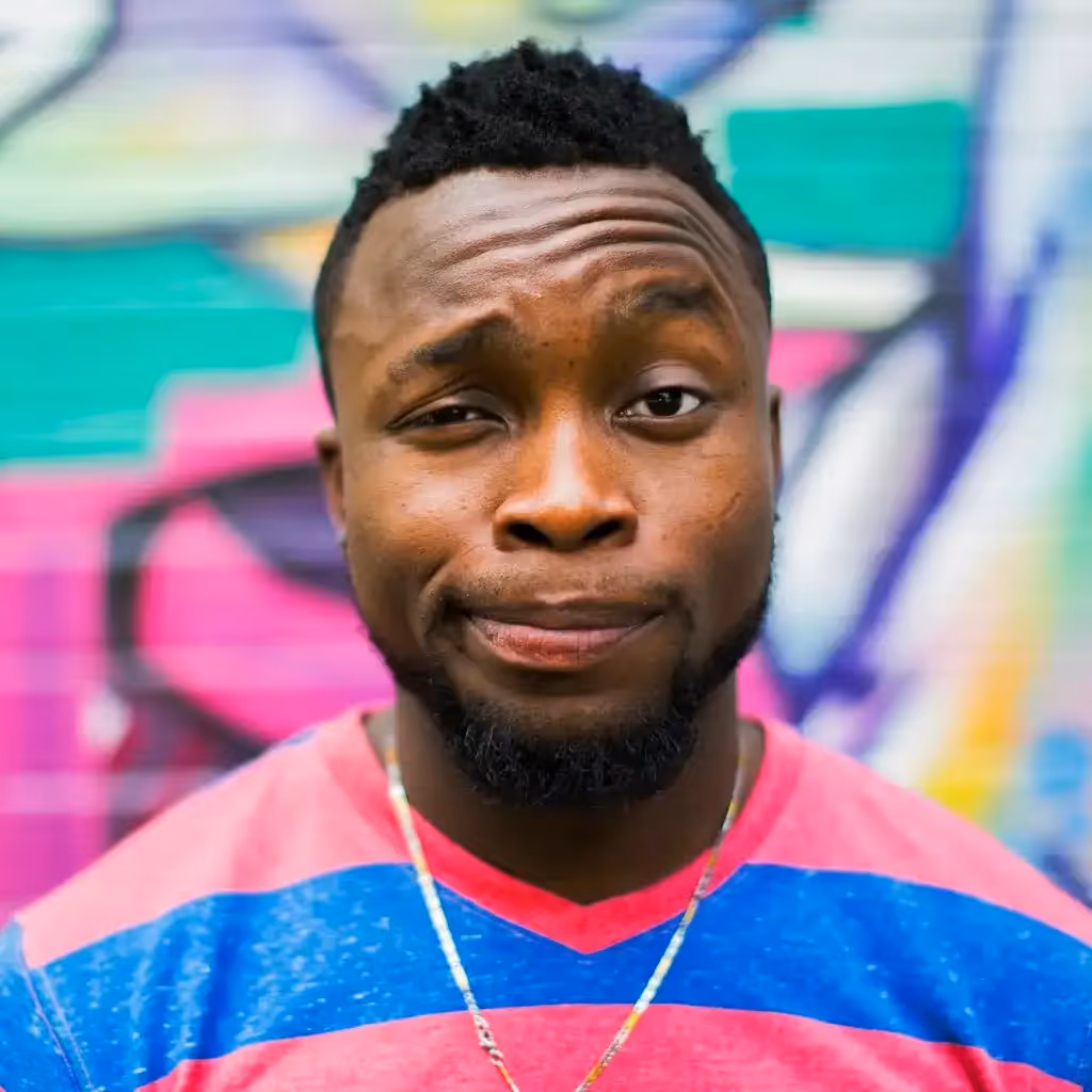 Un homme vêtu d'une chemise à rayures rouges et bleues prend un air espiègle et sceptique devant un fond de graffitis colorés. Le ton est léger et humoristique.