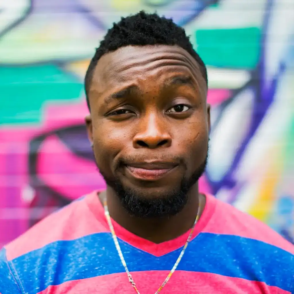 A man in a red and blue-striped shirt makes a playful, skeptical face against a colorful graffiti background. The tone is lighthearted and humorous.