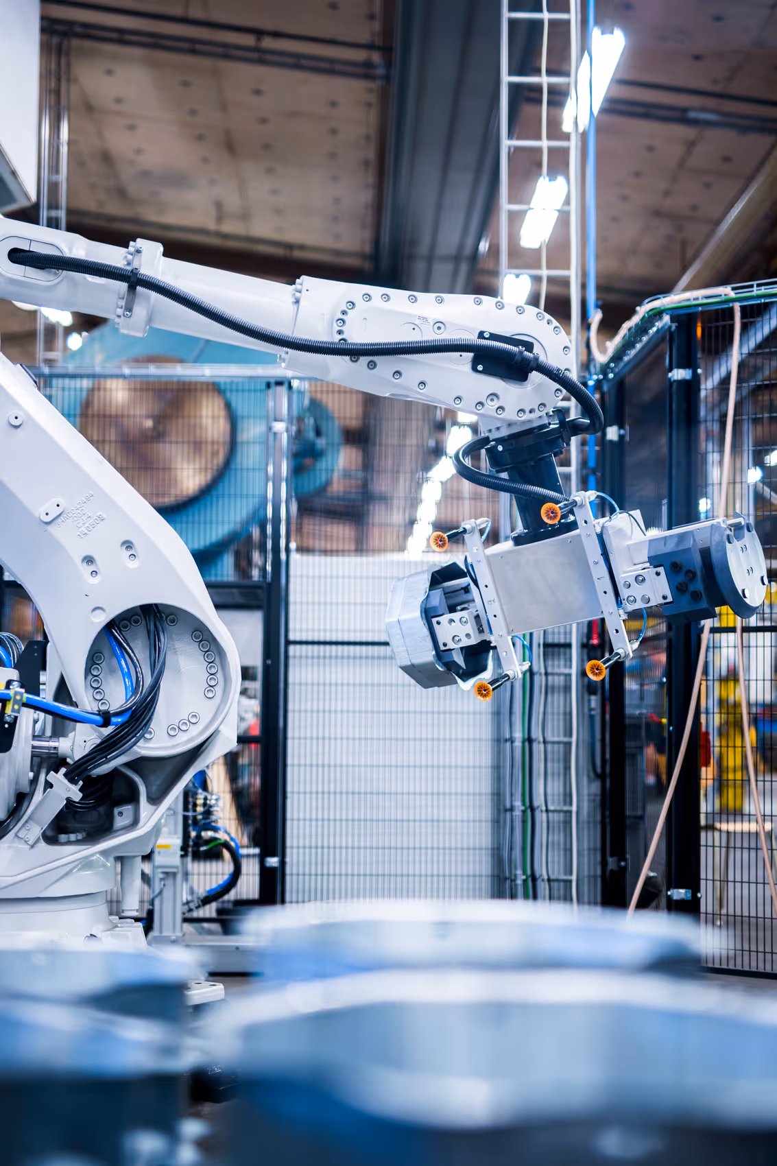 Close-up of a white industrial robotic arm operating in a modern factory setting with metal equipment in the foreground.