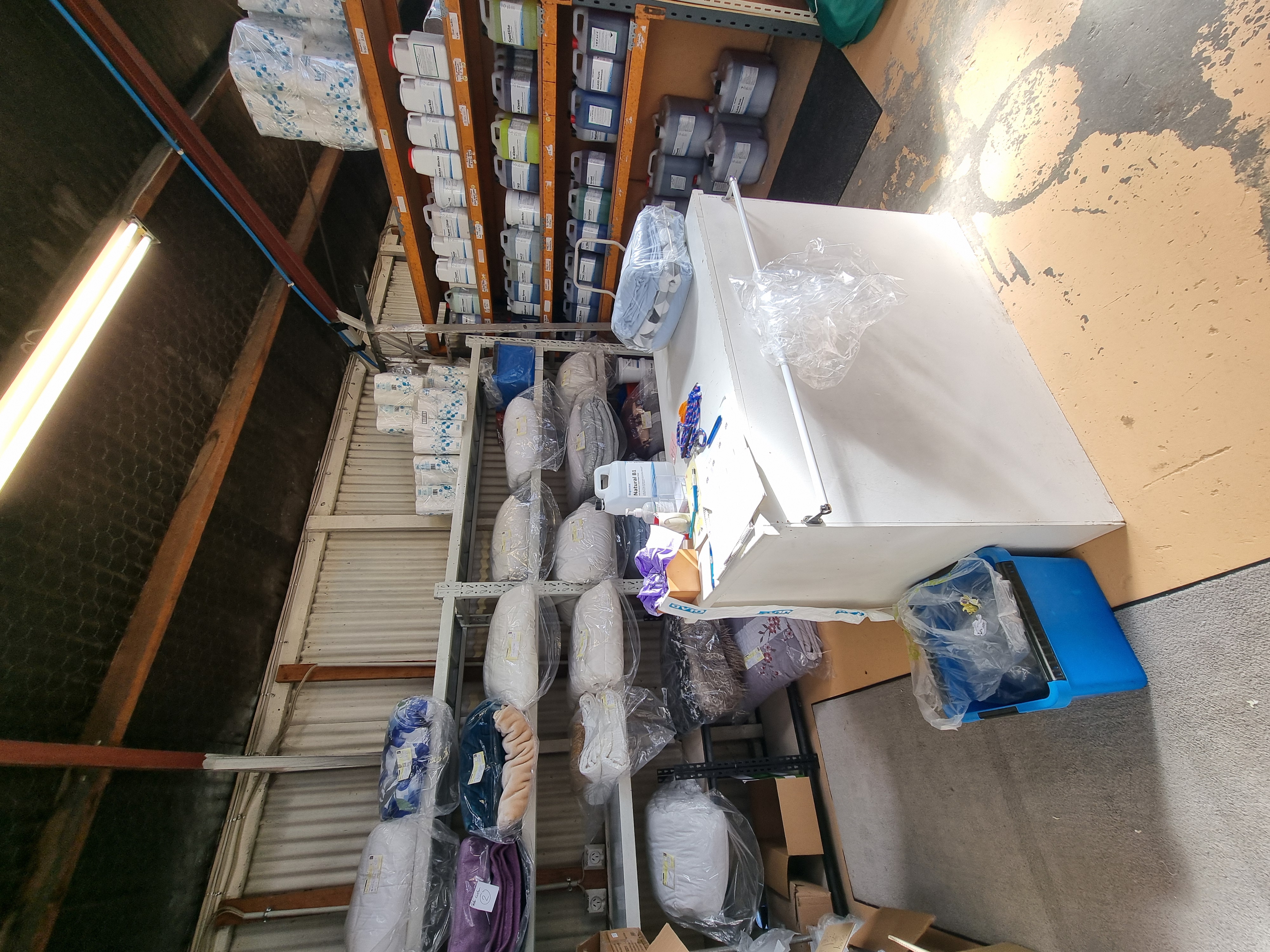 An area with cleaning supplies on the shelves and some folded laundry