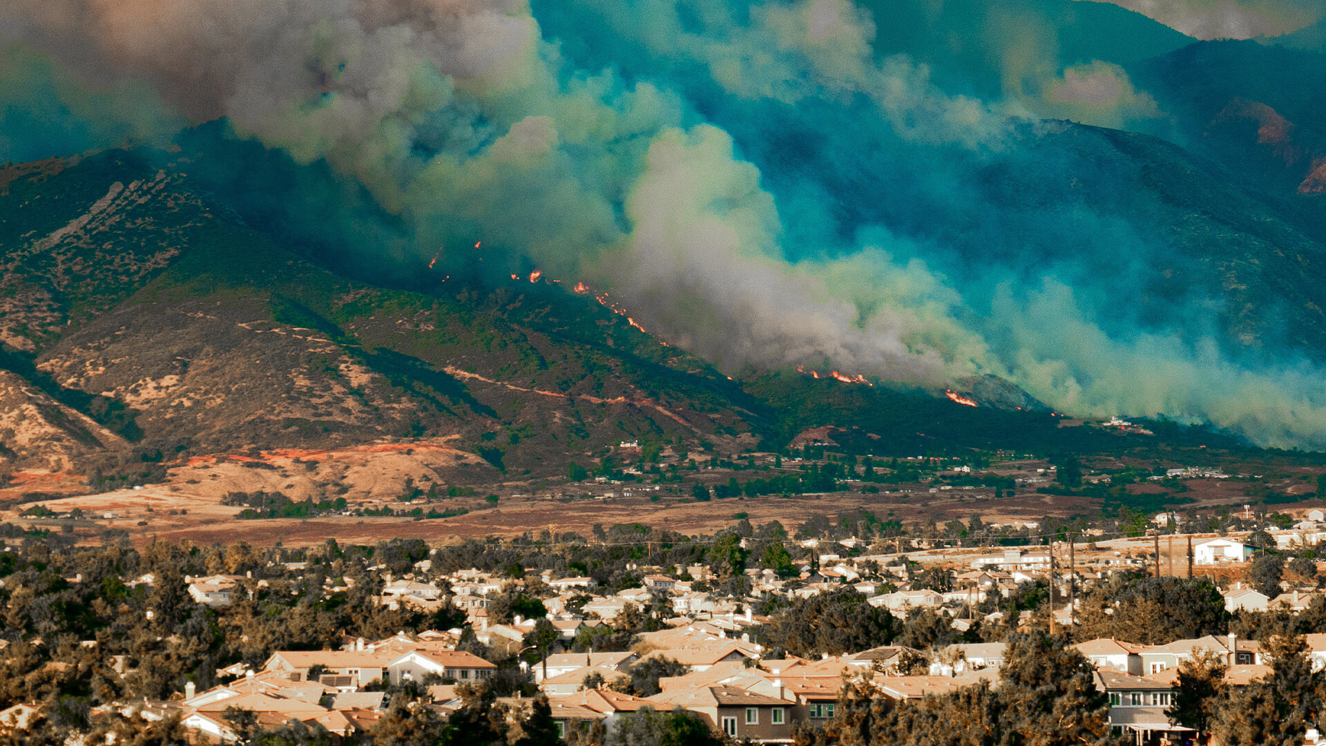 A wildfire on a hill bears down on the community below