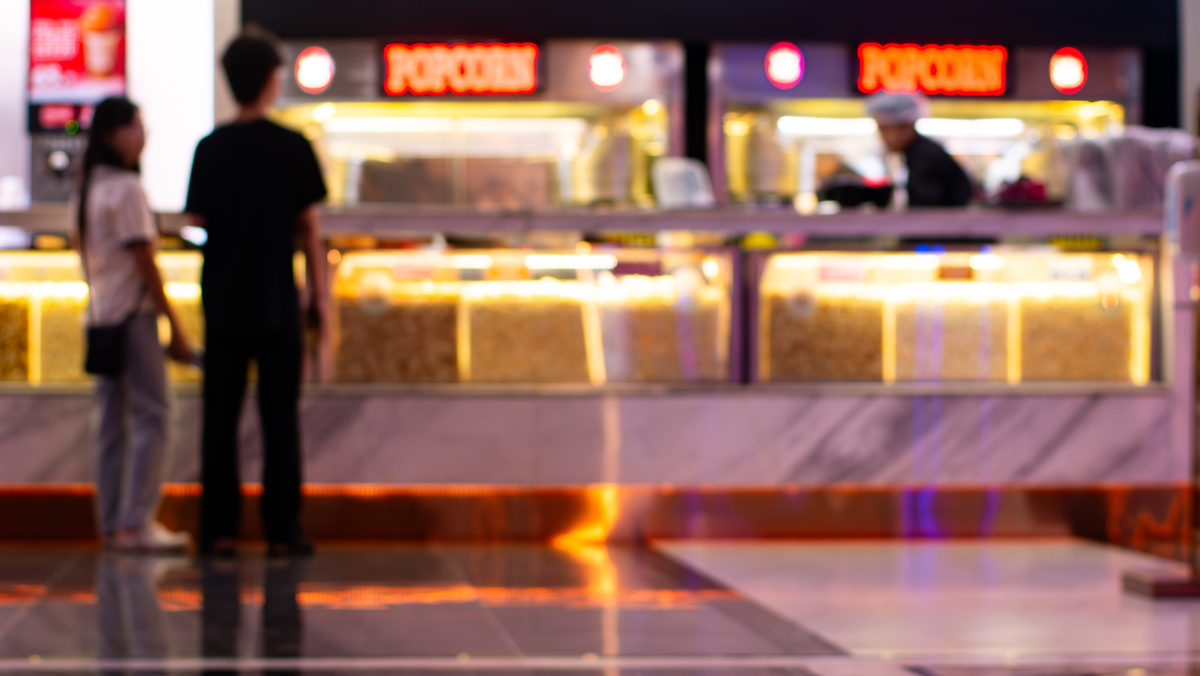 Guests ordering at a cinema concession stand with lit popcorn displays