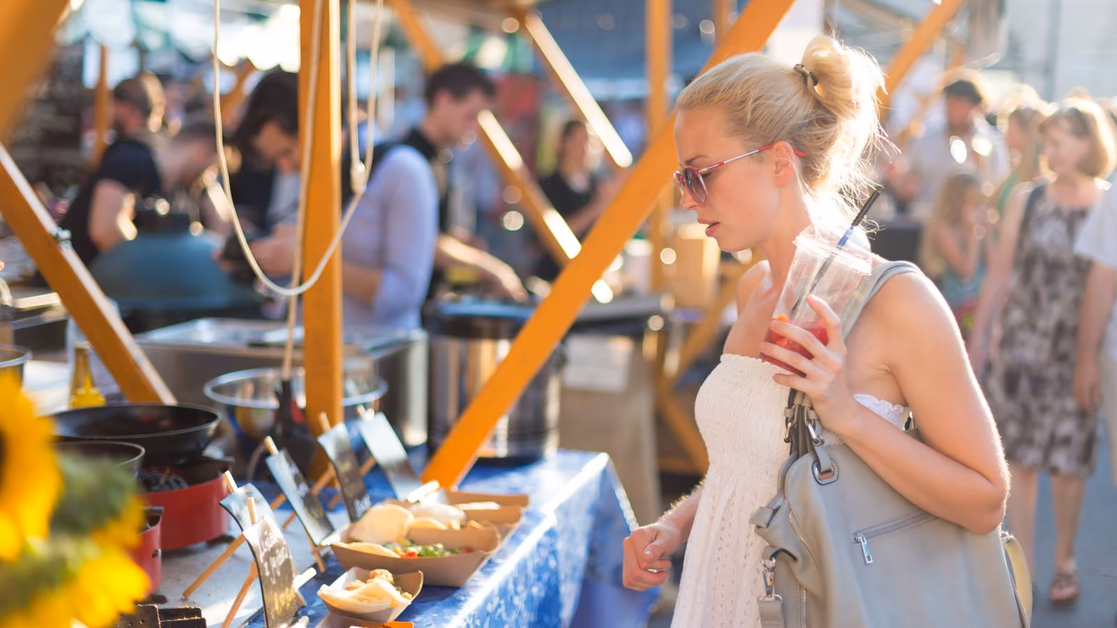 A guest choosing food at one of several independent vendor stalls in an open-air market where multiple businesses share one checkout.