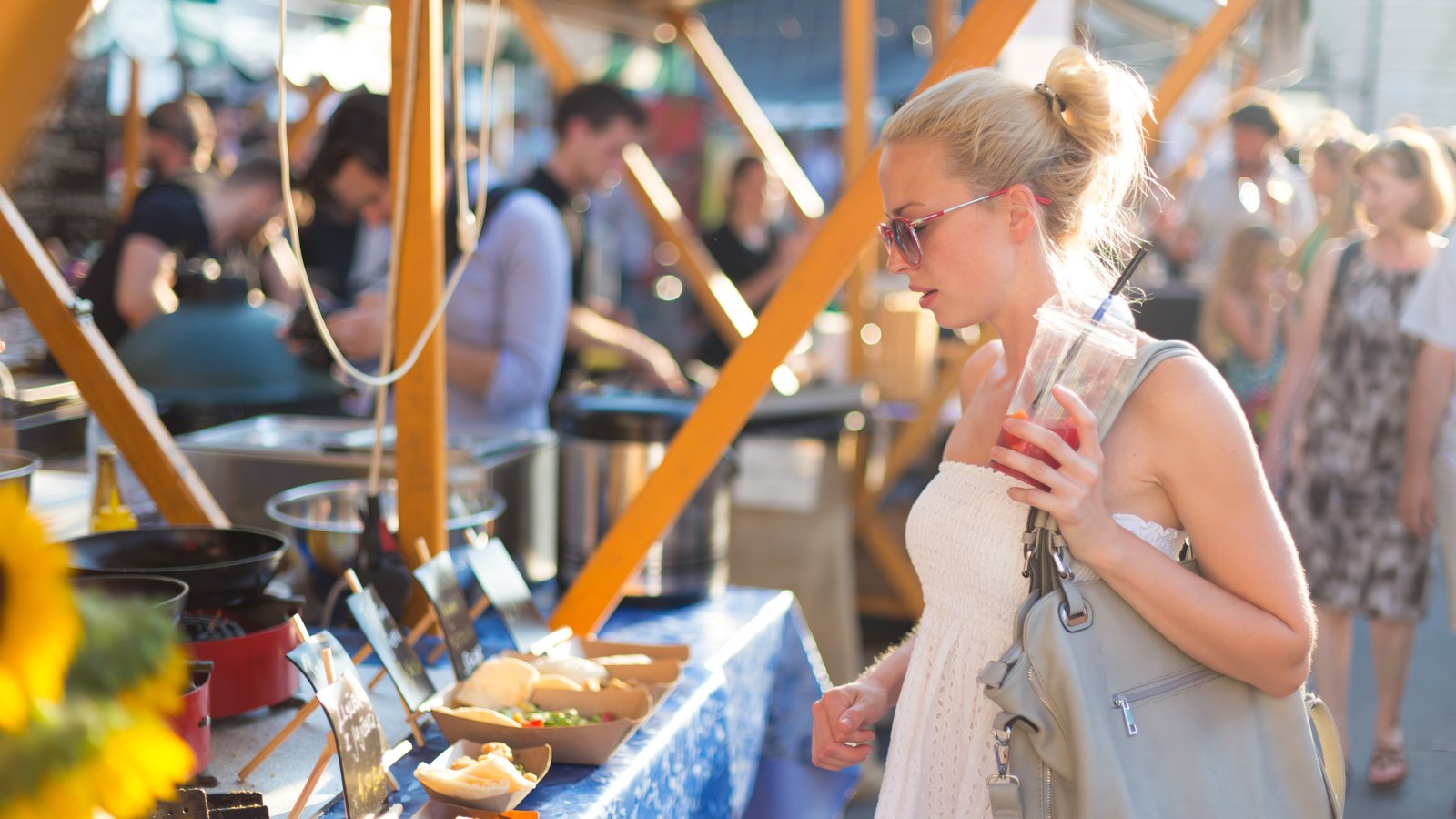 A guest choosing food at one of several independent vendor stalls in an open-air market where multiple businesses share one checkout.