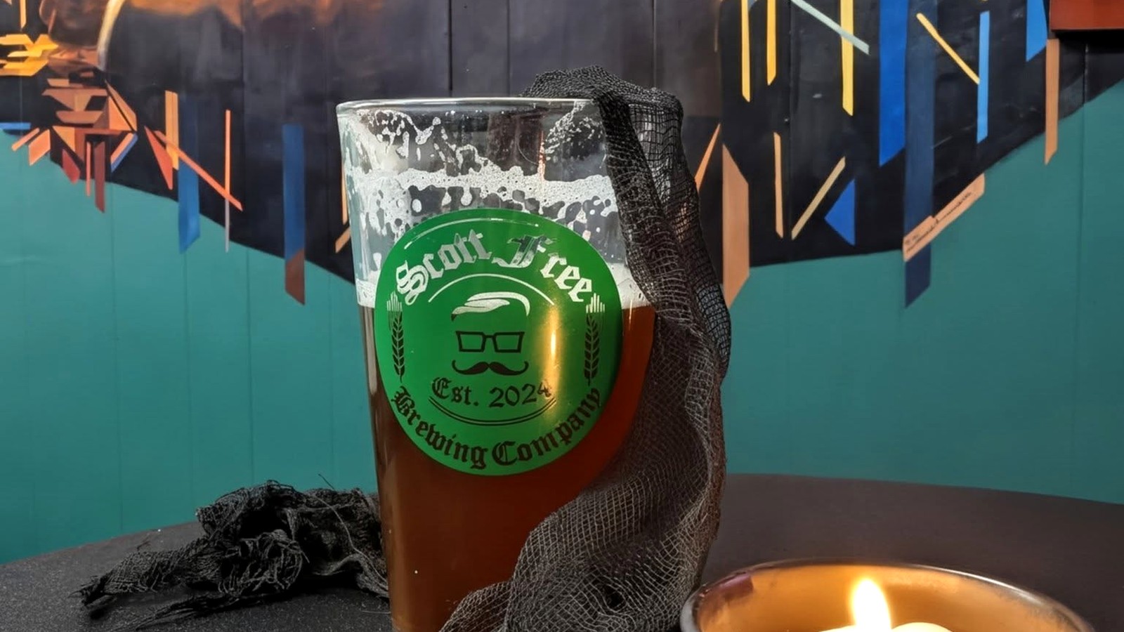 Una pinta de cerveza de Scott Free Brewing en un vaso de la marca frente al mural del taproom en Scottsbluff, Nebraska.