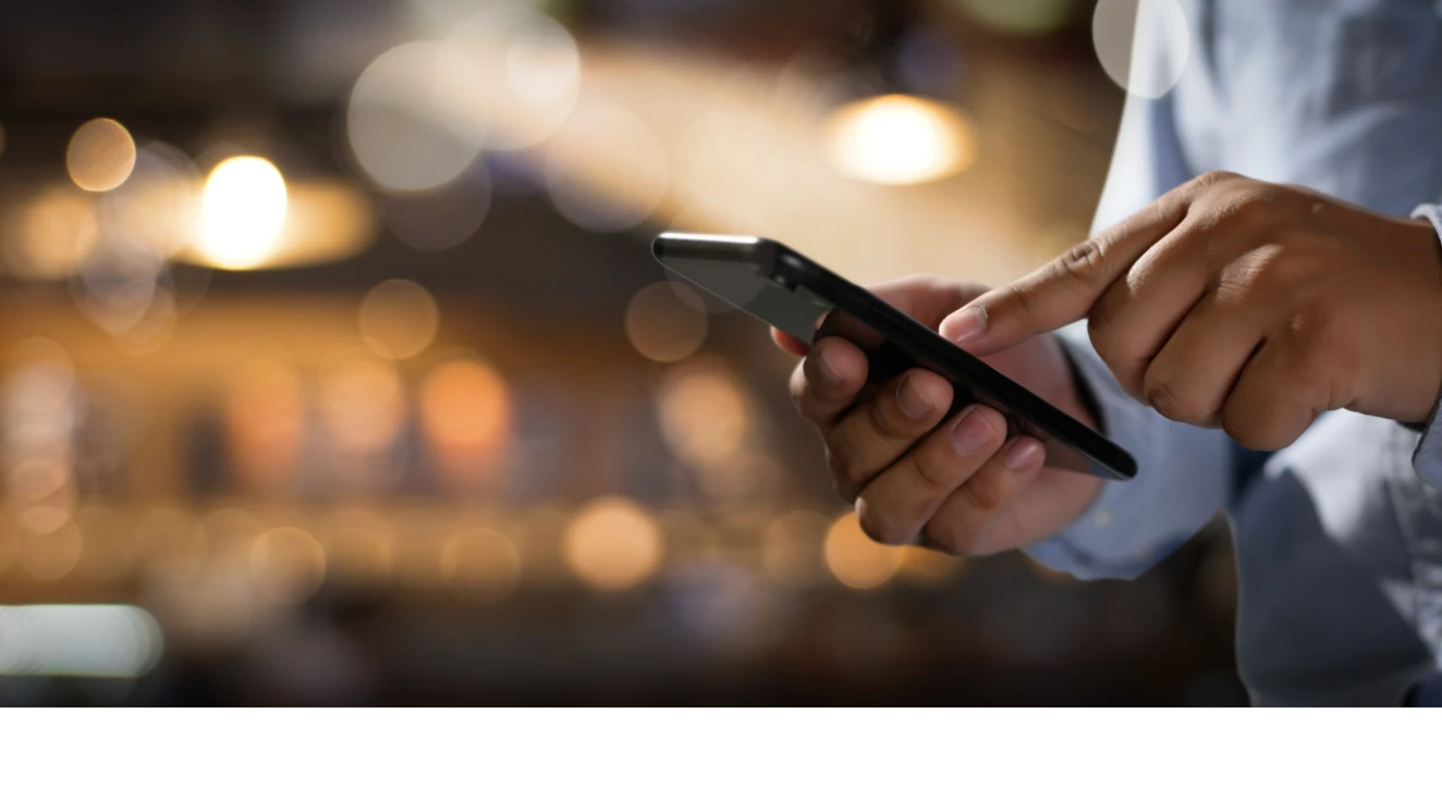 A bartender using an iPhone behind a bar