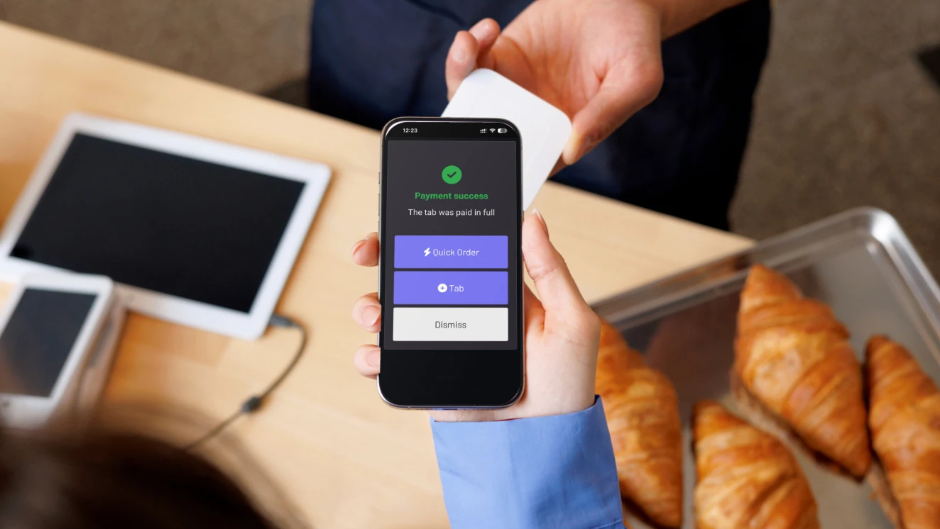 An iPhone showing a GoTab payment confirmation held at a cafe counter