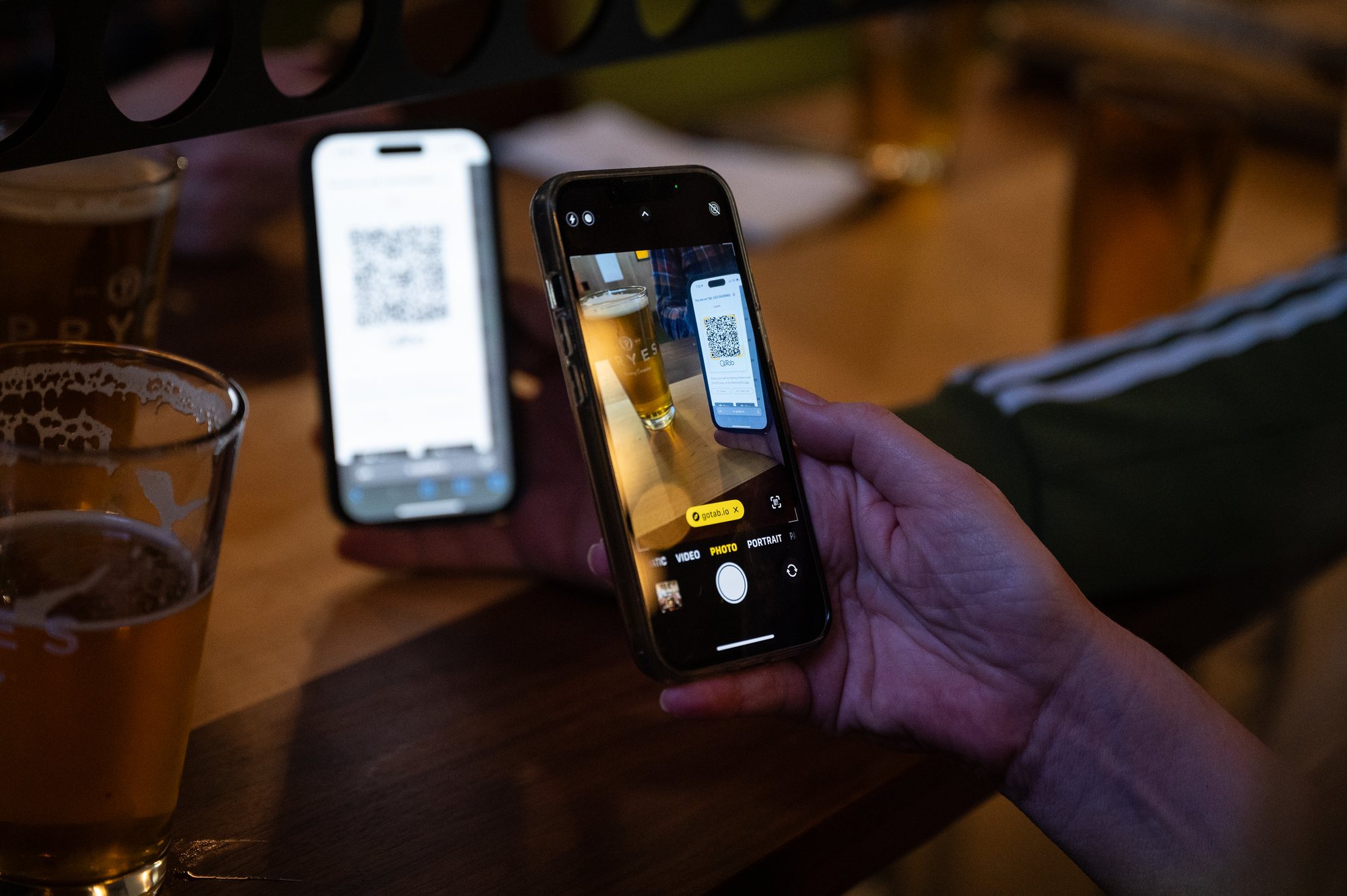 A guest scans a QR code with their phone to open a tab at a brewery bar, a glass of beer in the foreground.