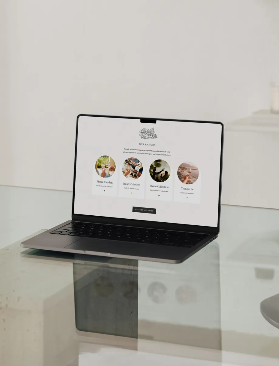 Open laptop on a glass table displaying a website page with four wine range options: Pierre Jourdan, Haute Cabrière, Haute Collection, and Tranquille.