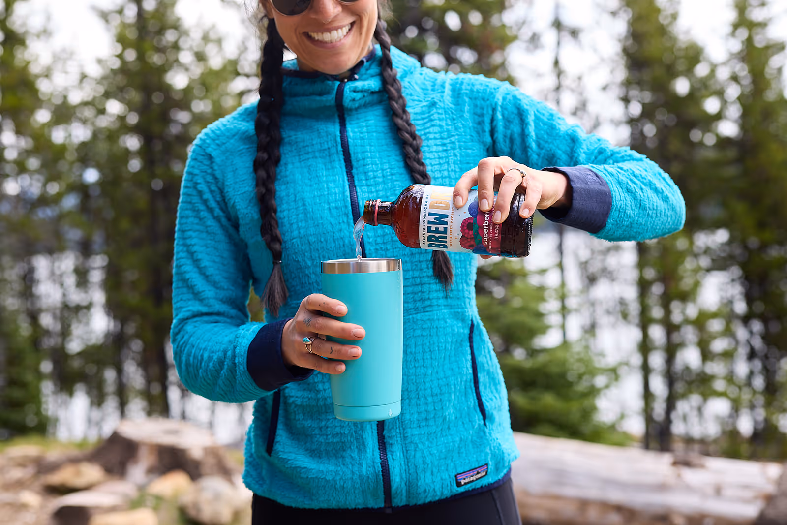 Person pouring a bottle of organic Brew Dr. Superberry kombucha into an insulated mug
