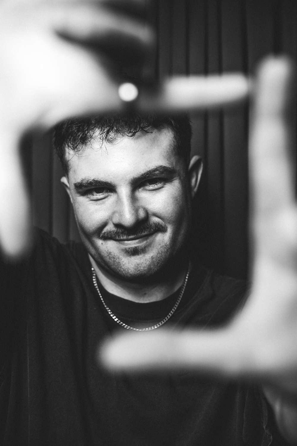 Smiling man with short hair and mustache framing his face with his hands in black and white photo.