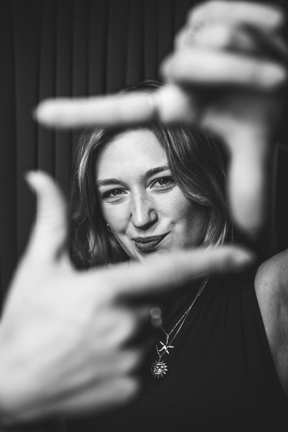 Black-and-white photo of a woman framing her face with her hands, smiling slightly.
