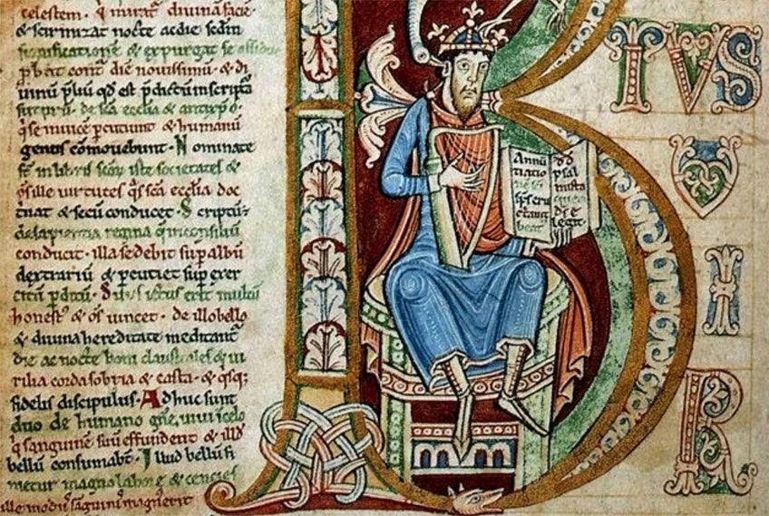 Eine illuminierte Manuskriptseite mit einem großen, verzierten Anfangsbuchstaben „B“, der eine sitzende, gekrönte Figur rahmt, die Harfe spielt und ein offenes Buch hält. Der Hintergrund und die Ränder sind mit komplizierten mittelalterlichen Flechtwerkmustern und lateinischer Schrift in schwarzer Tinte mit roten Akzenten gefüllt.