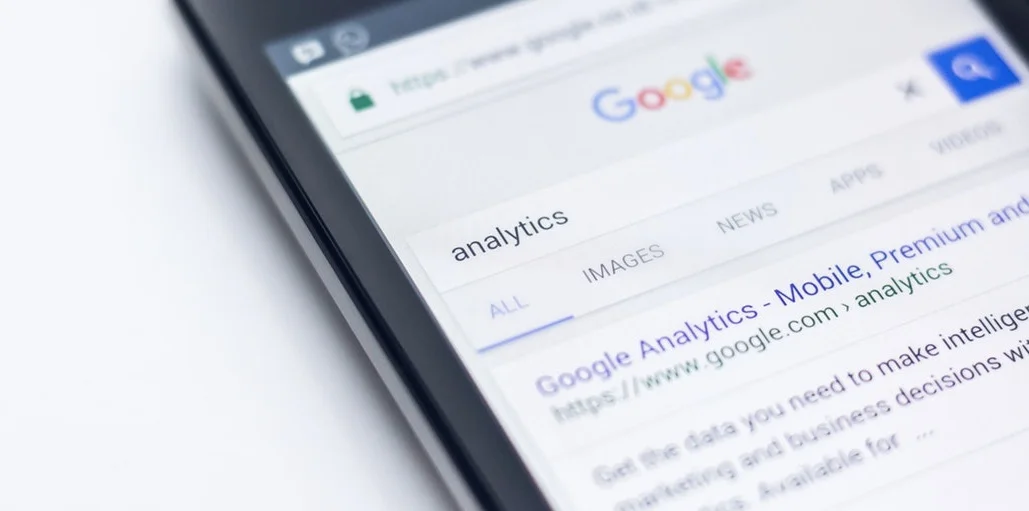 Nahaufnahme eines Smartphone-Bildschirms mit einer Google-Suche nach dem Wort „analytics“, wobei das erste Suchergebnis für Google Analytics sichtbar ist.